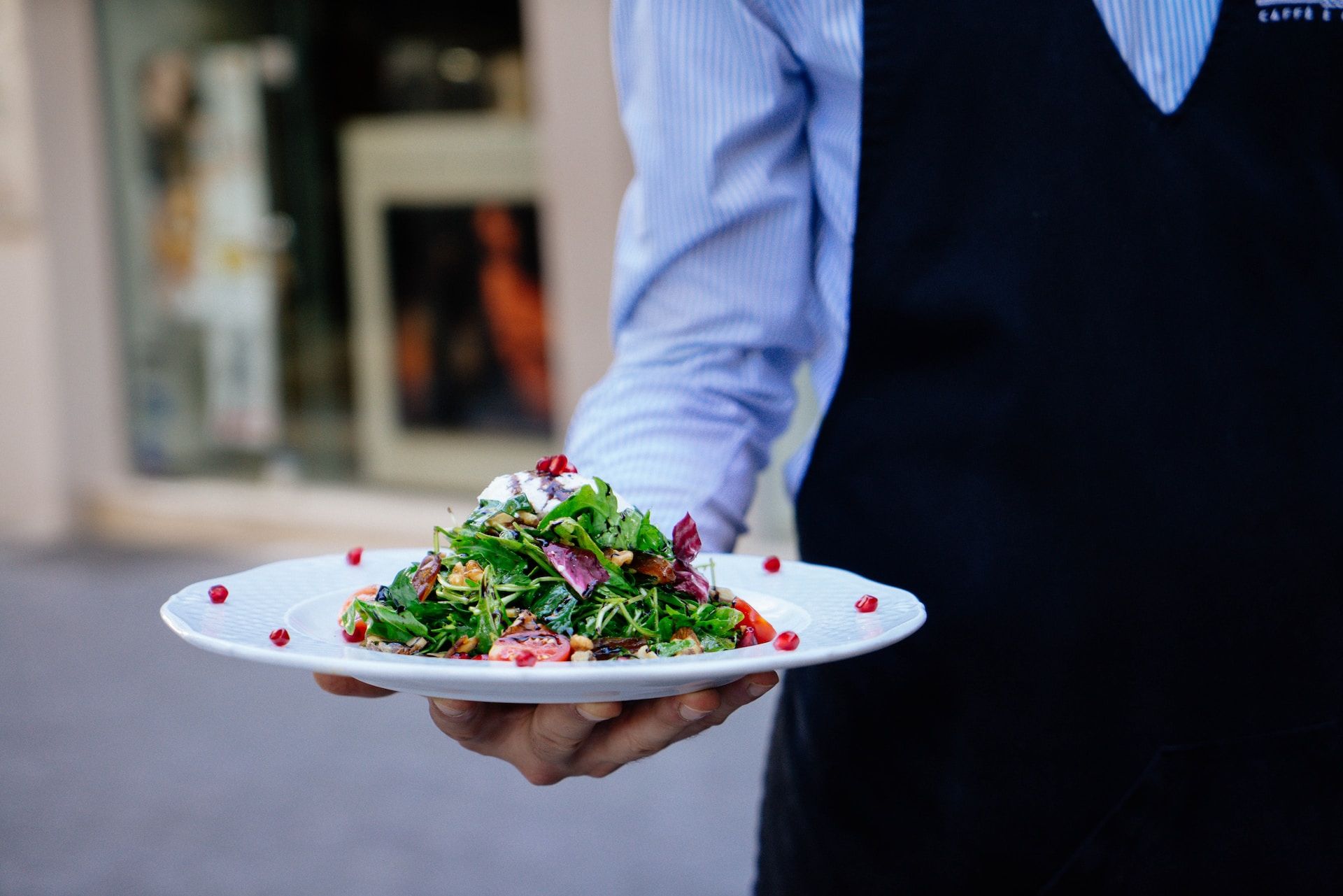 right arm of a waitor, holding a white plate with nicely arranged mixed salad