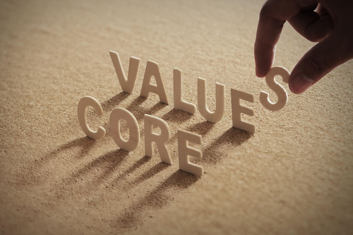 CORE VALUE wood word on corkboard with human's finger at S letter.